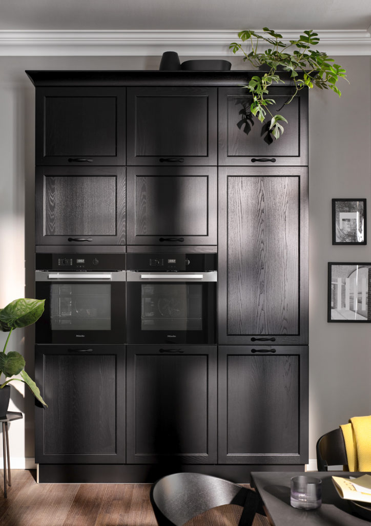 Muebles negros en columna en cocina de estilo clásico con molduras y tiradores cortos negros.