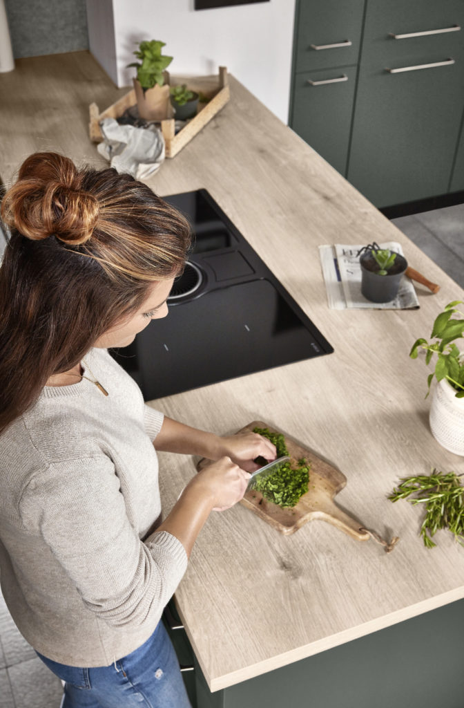 Mujer cortando perejil en la zona de trabajo de la isla de cocina