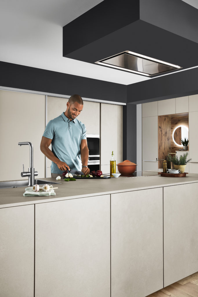 Hombre joven cocinando en isla con zona de trabajo, zona de cocción y zona de lavado.