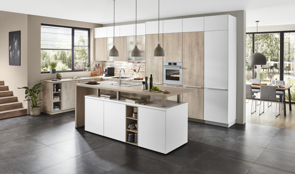 Cocina en forma de L con isla con espacio de almacenaje. Cocina de color madera natural y blanco mate con tirador integrado.