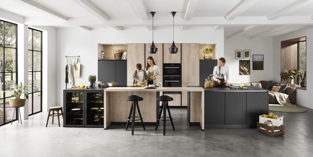 Familia cocinando en una preciosa y gran cocina de acabado madera clara y negro mate. Cocina con electrodomésticos integrados.