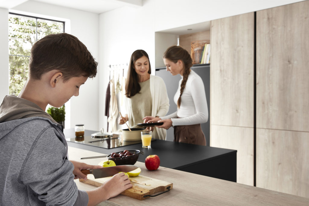 Familia feliz cocinando en cocina con isla con zona de trabajo y zona de cocción