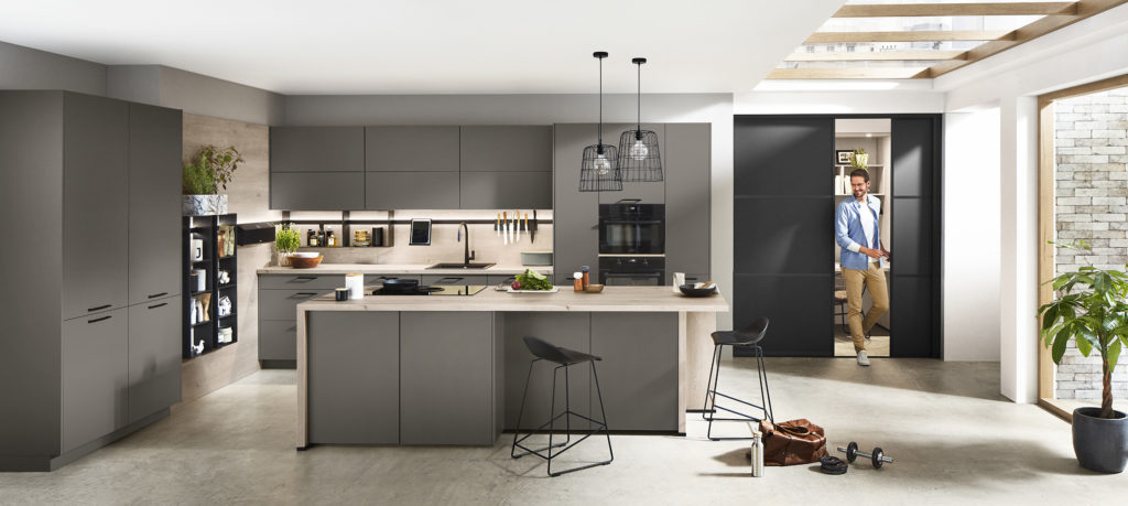 Cocina abierta con isla de acabado gris perlado y madera clara natural.