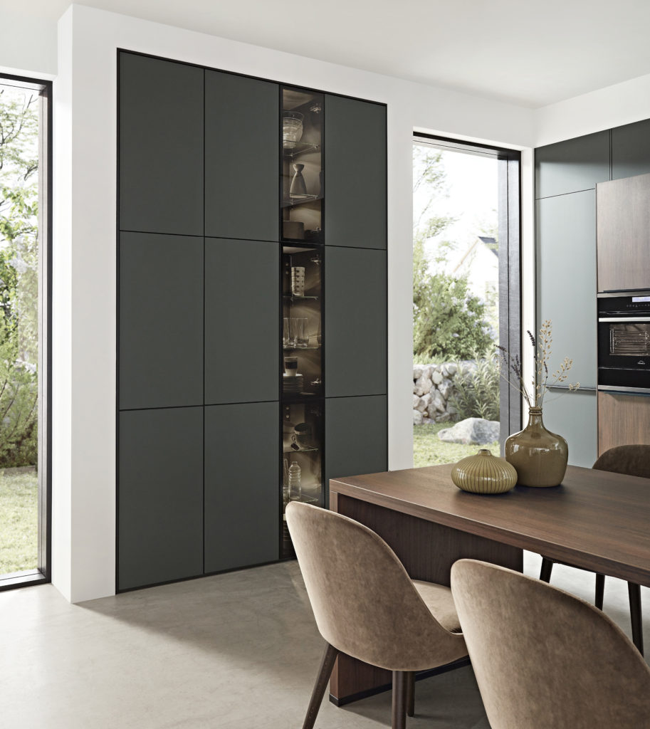 Mueble columna hecho a medida en cocina moderna de acabado verde esmeralda con vitrina de cristal oscuro.